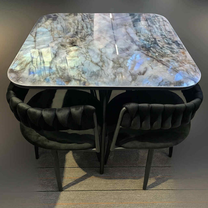 Quatre fauteuils noirs tressés autour d’une table carrée à plateau en labradorite. Quatre fauteuils noirs tressés autour d’une table carrée à plateau en labradorite.